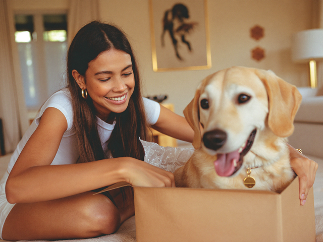 Lächelnde Frau packt gemeinsam mit ihrem Hund ein Geschenk mit royalem Hundeportrait aus