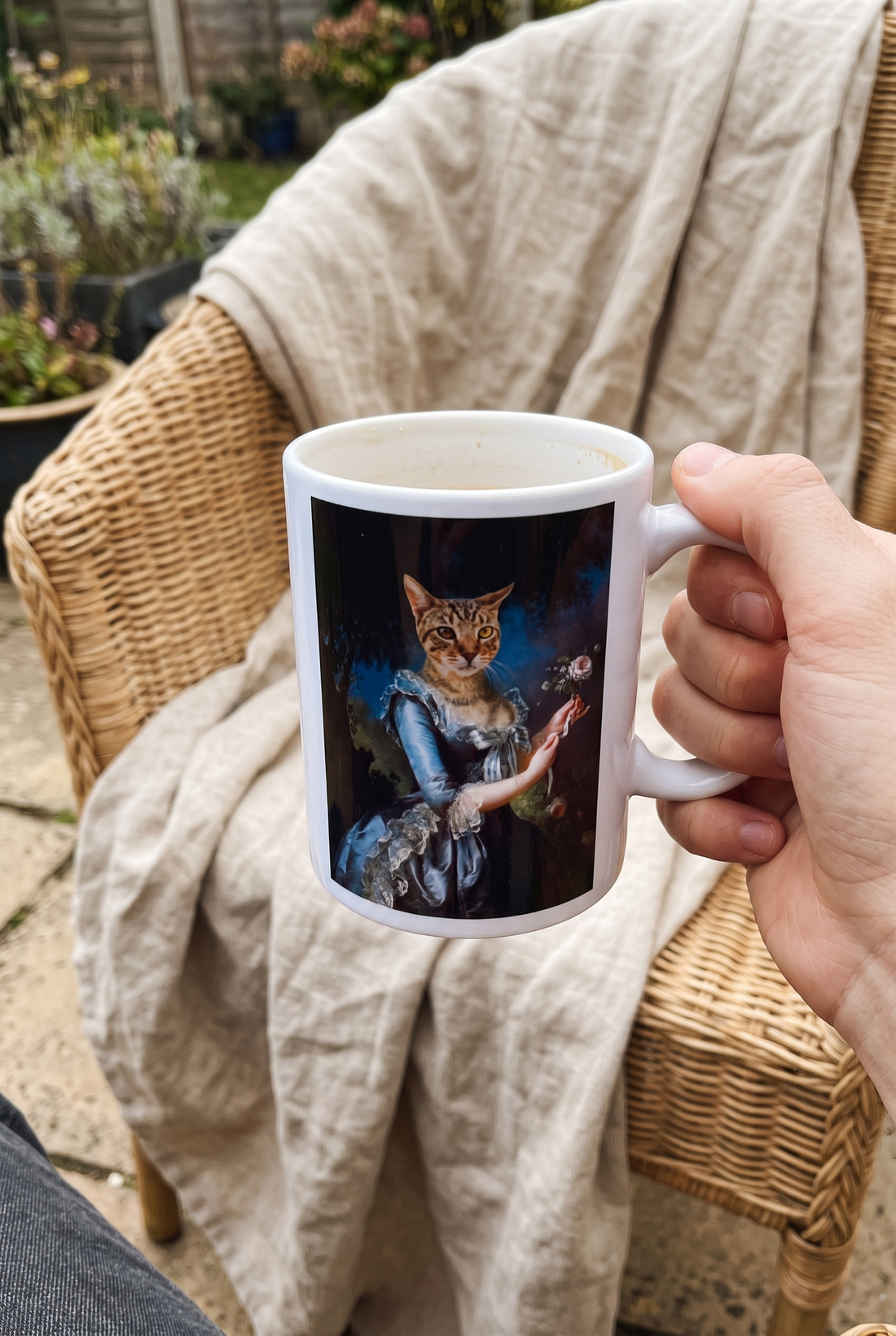 Personalisierte Tasse mit Katze als Prinzessin in der Hand auf einem Korbsessel