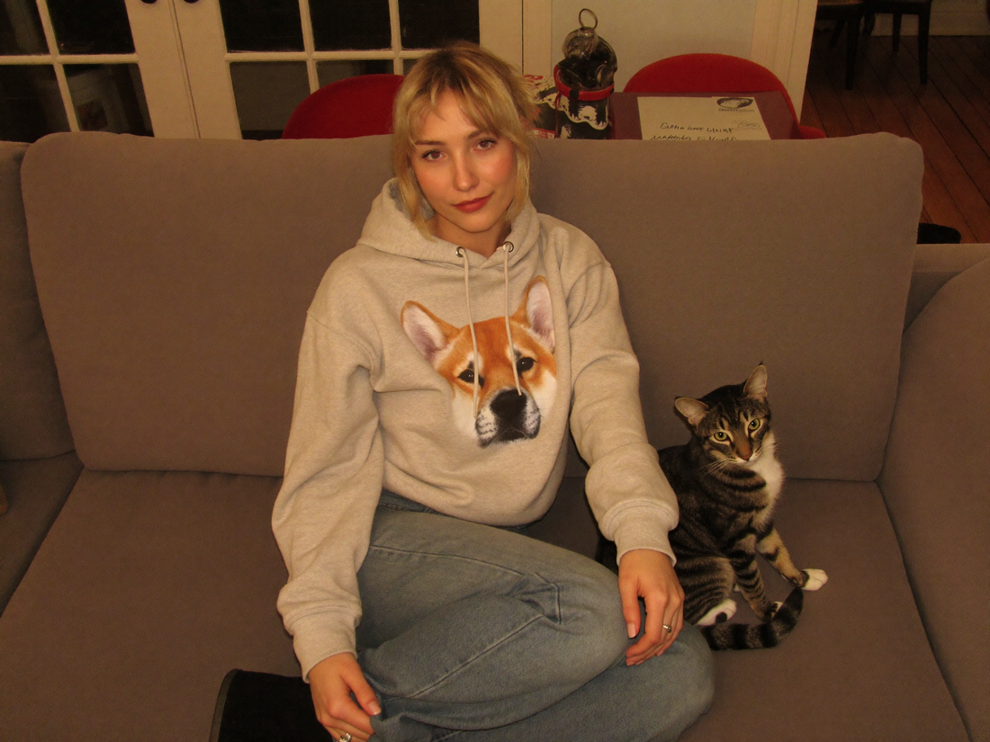Frau traegt Hoodie mit Haustier-Portrait, Hund und Katze im Wohnzimmer