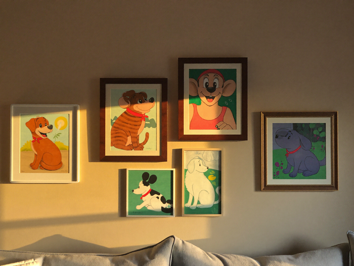 Verschieden grosse gerahmte Haustierportraits an einer Wohnzimmerwand, Disney-Illustration