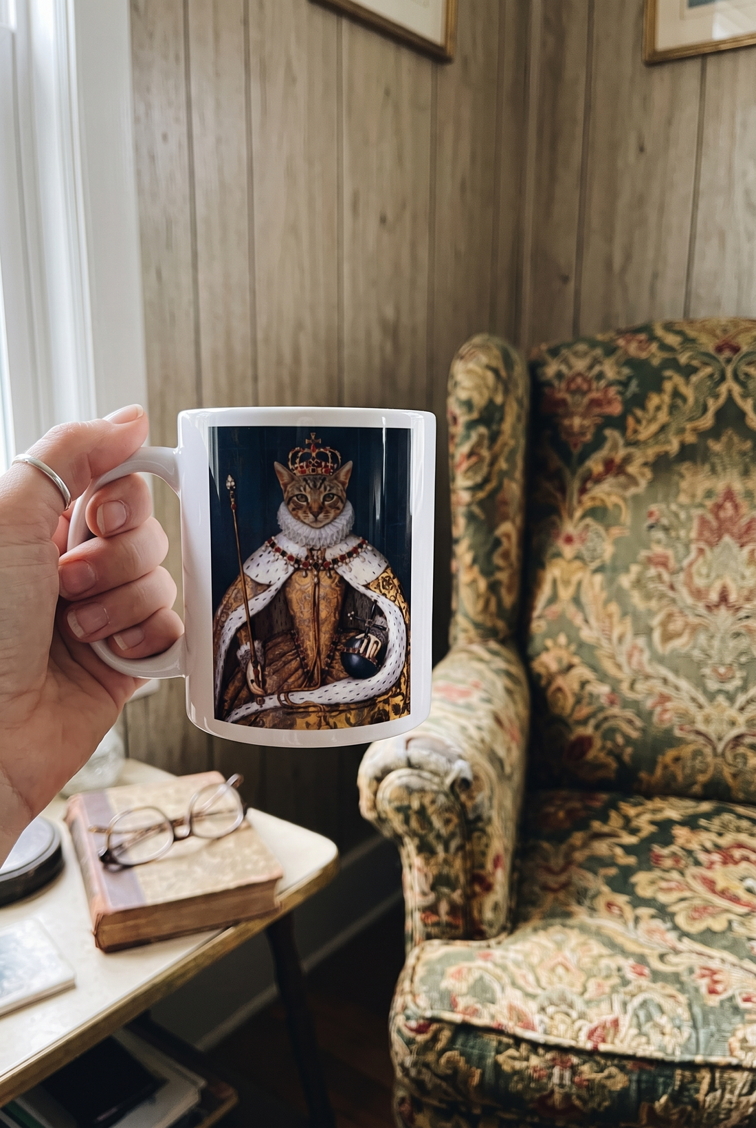 Personalisierte Tasse mit Katze als Koenigin in der Hand neben einem Gobelinsessel