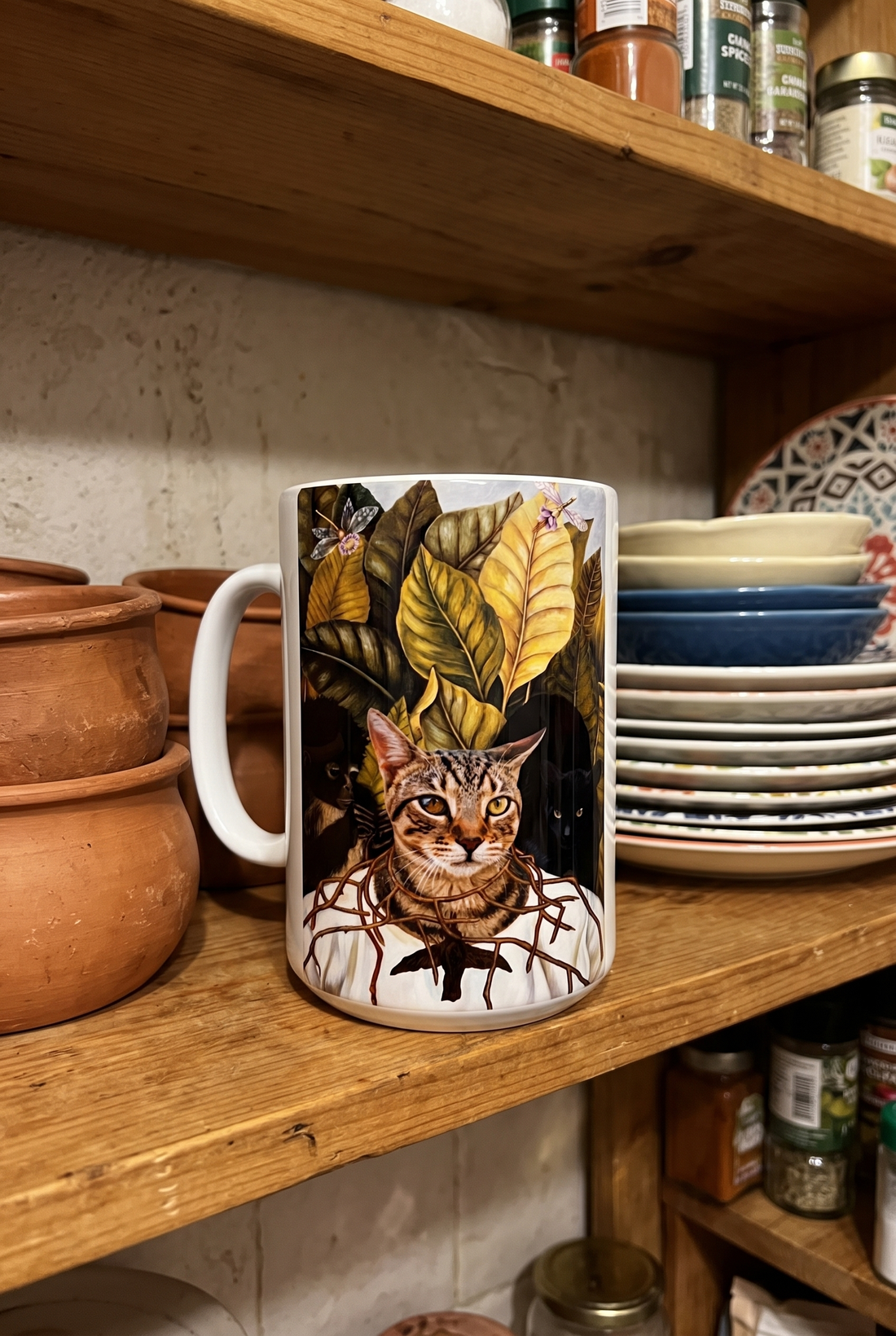 Bunte Tasse mit Katze auf einem Kuechenregal zwischen Tontoepfen