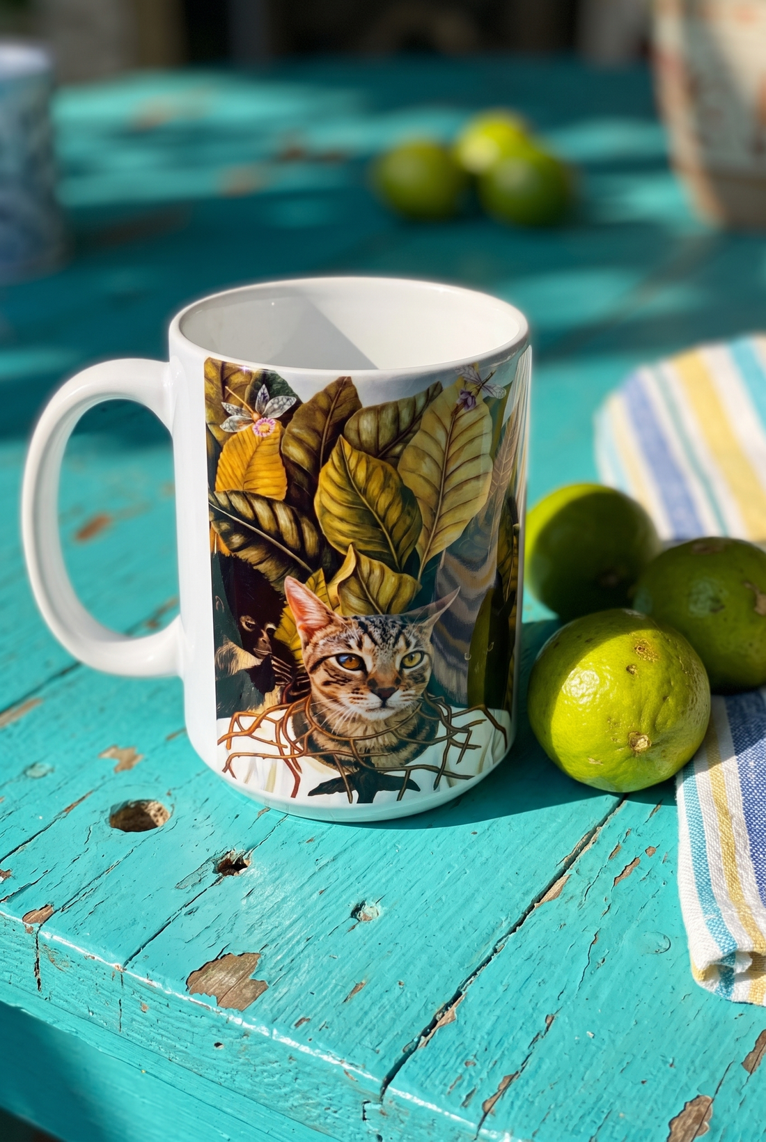 Bunte Tasse mit Katze auf einem tuerkisen Holztisch neben Limetten